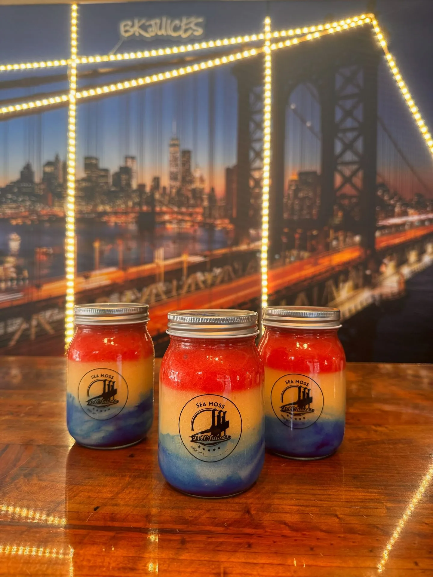 BK Juices sea moss jars with colorful fruit layers in front of the Brooklyn Bridge